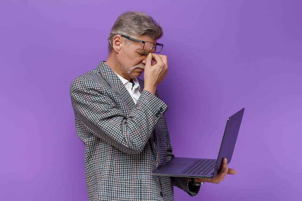 Hombre se restriega los ojos frente a un portátil tras cometer errores en las redes sociales