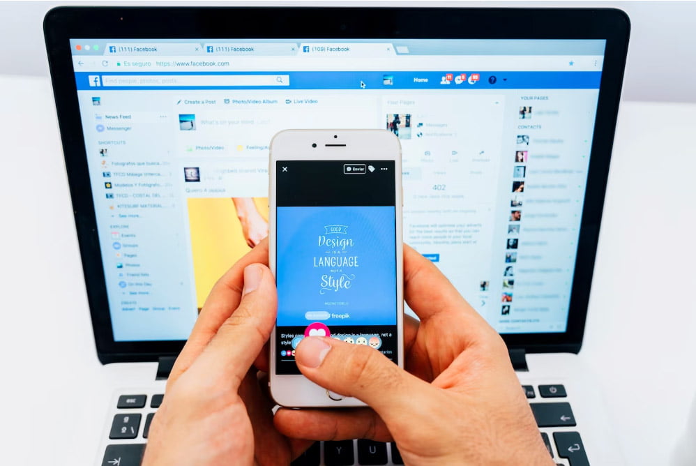 Una persona da like en su móvil mientras navega en Facebook en su PC, una de las redes sociales horizontales más importantes.