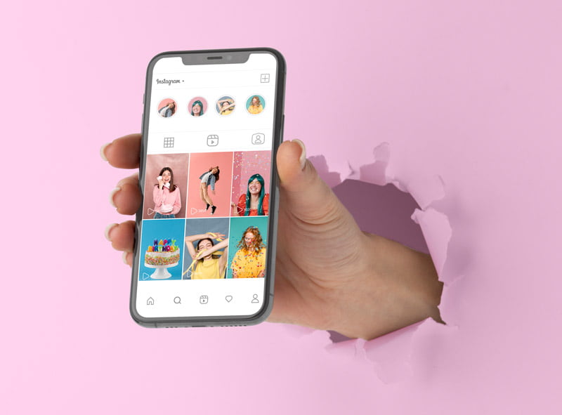 Mano sobresale de un mural de papel rosa con el móvil en la mano en un perfil de Instagram.