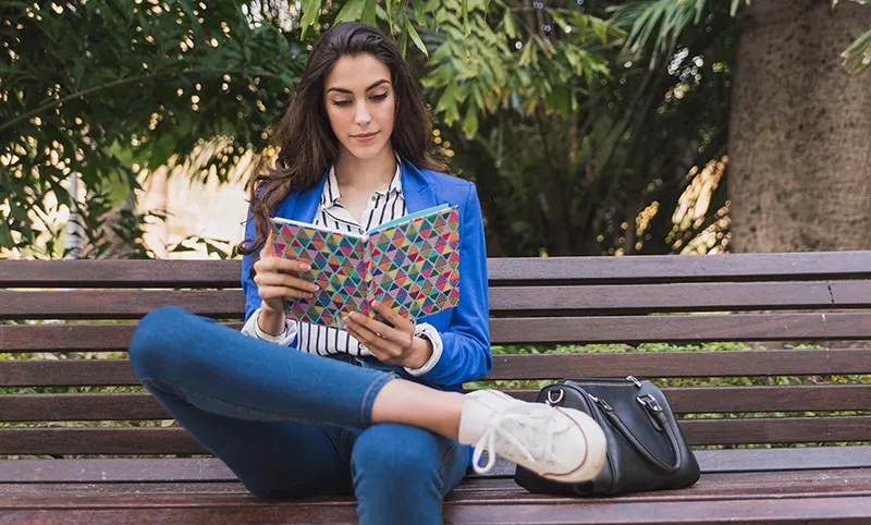 Emprendedor o empresaria sentada en un banco leyendo en una libreta los libros de marketing digital para emprendedores y profesionales que se había apuntado del blog de garajedoce. 